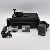 Gray action camera with waterproof case and mounting accessories, plus black storage case.
