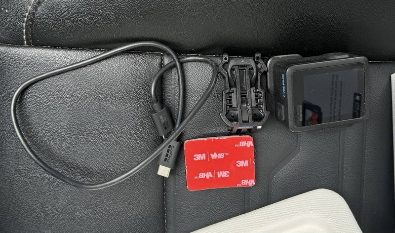 Black action camera kit with mounting bracket, cables, and adhesive tabs