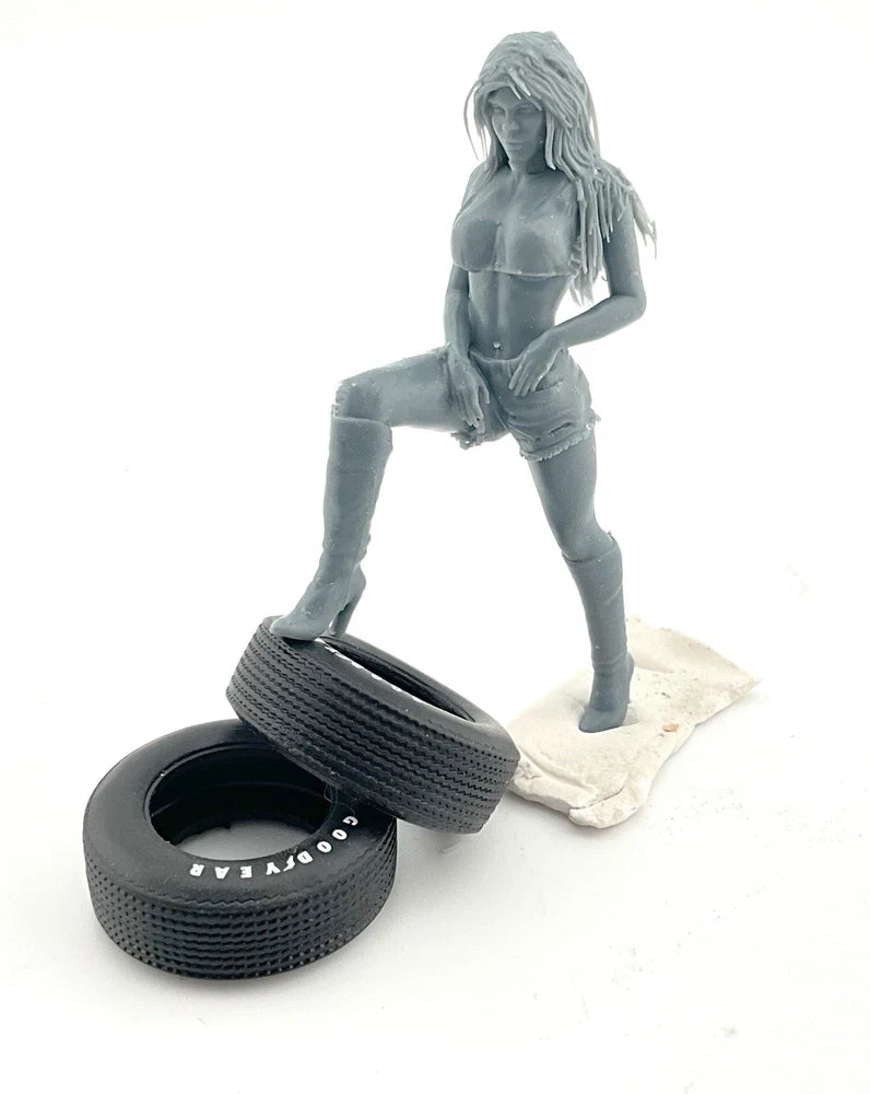 Gray kneeling female scale model figure with two large tires at front