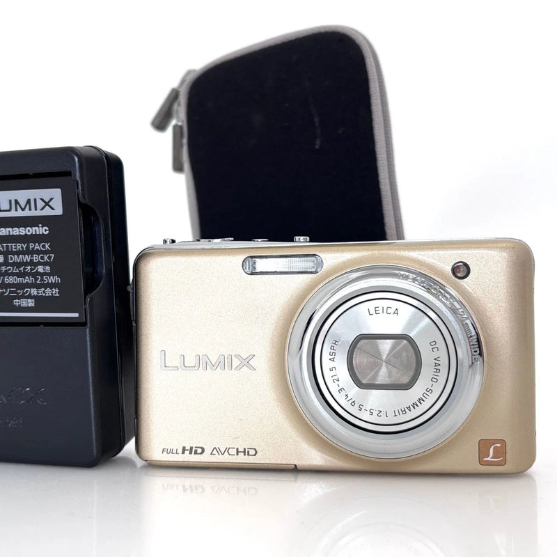 Gold compact digital camera with LUMIX lens and front control panel, shown with case