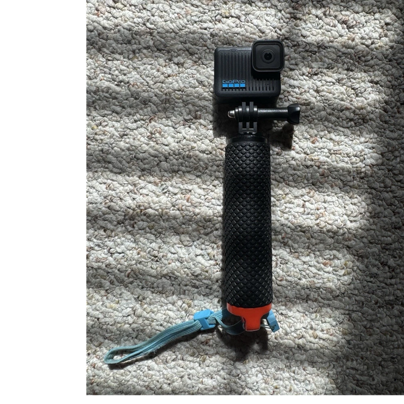 Black action camera on textured handheld grip mount, with side USB-C port visible.