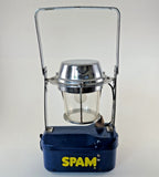 Blue battery lantern with clear glass chimney and chrome top, SPAM logo on base.