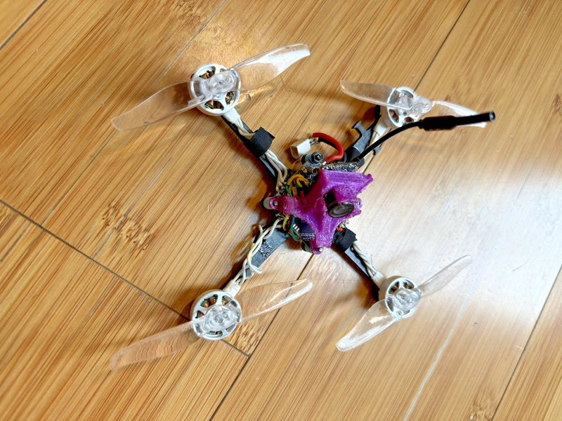 Small purple FPV quadcopter drone with four propellers and exposed electronics