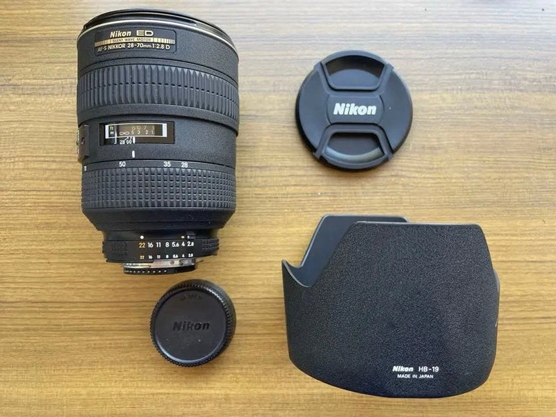 Black Nikon zoom lens with front and rear caps and lens hood
