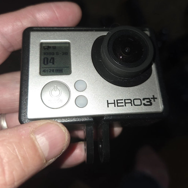 Silver action camera with black lens and HERO3+ logo, front buttons and status screen