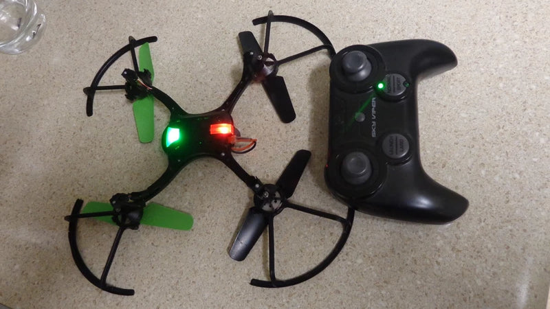 Black quadcopter drone with green/red LEDs and black controller