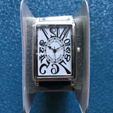 Square-faced chronograph watch with white dial, black Roman numerals, and black hands