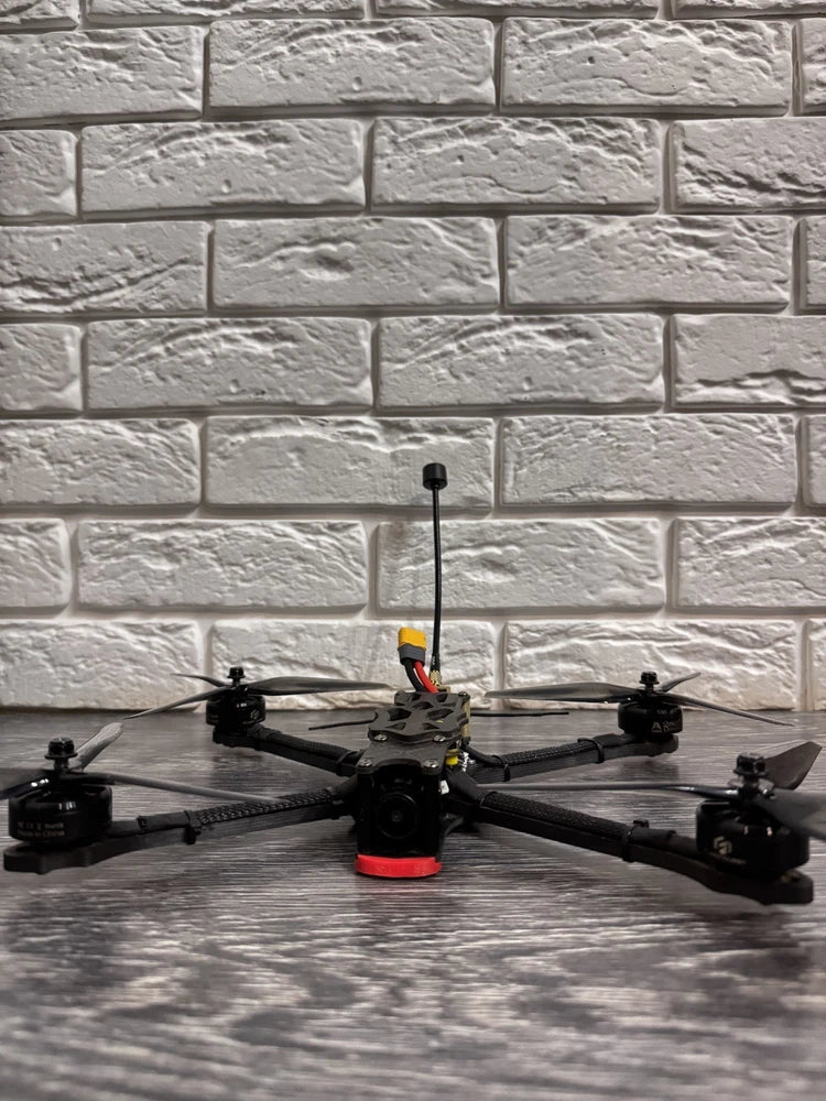 Black FPV quadcopter drone with central orange frame and antenna mast