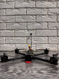 Black FPV quadcopter drone with central orange frame and antenna mast