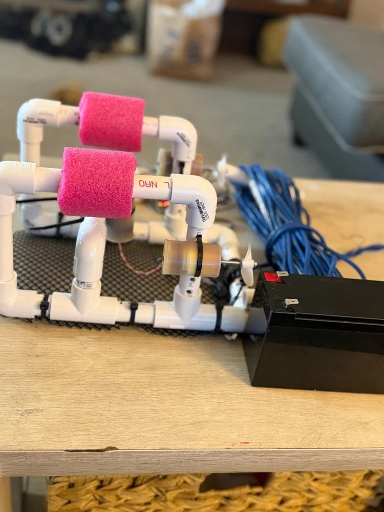 Underwater drone with white frame and pink foam rollers, with visible cables and sensors