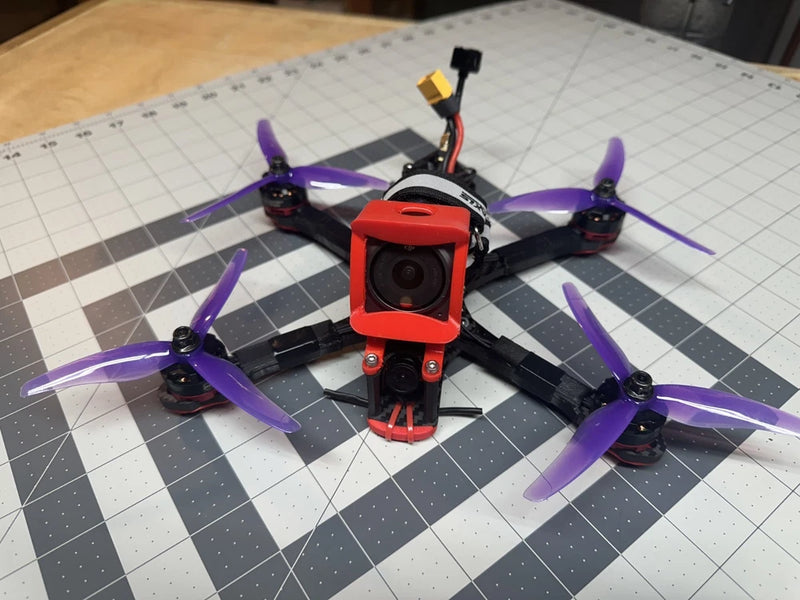 Freestyle FPV drone with red camera mount and purple propellers on black frame.
