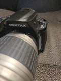Pentax K-30 DSLR camera with black body and attached zoom lens, side view.