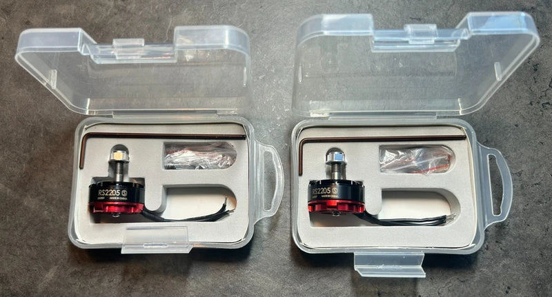Pair of FPV brushless drone motors in clear plastic storage cases with wires