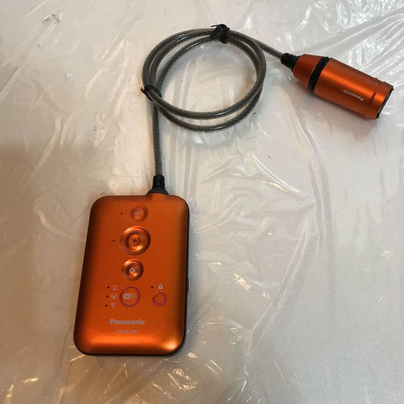 Orange Panasonic wearable camera with wrist remote, lens module, and black connecting cable