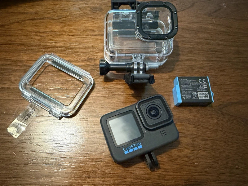 Black action camera with clear dive housing, open back door, and battery pack