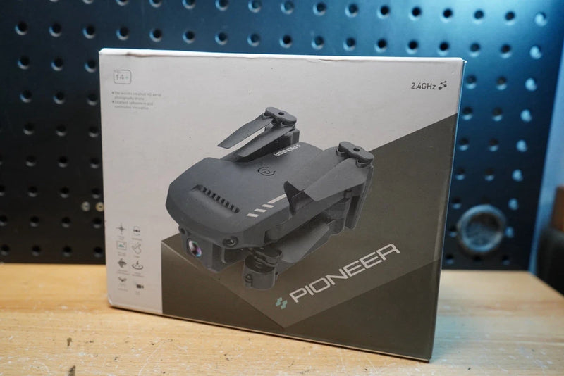 Black quadcopter drone shown on retail box, top view of 4-rotor frame