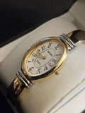 Oval gold-tone bangle quartz watch with white dial, Roman numerals, blue accents and curved strap