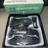 Black quadcopter drone with camera, folded arms and remote controller in open box