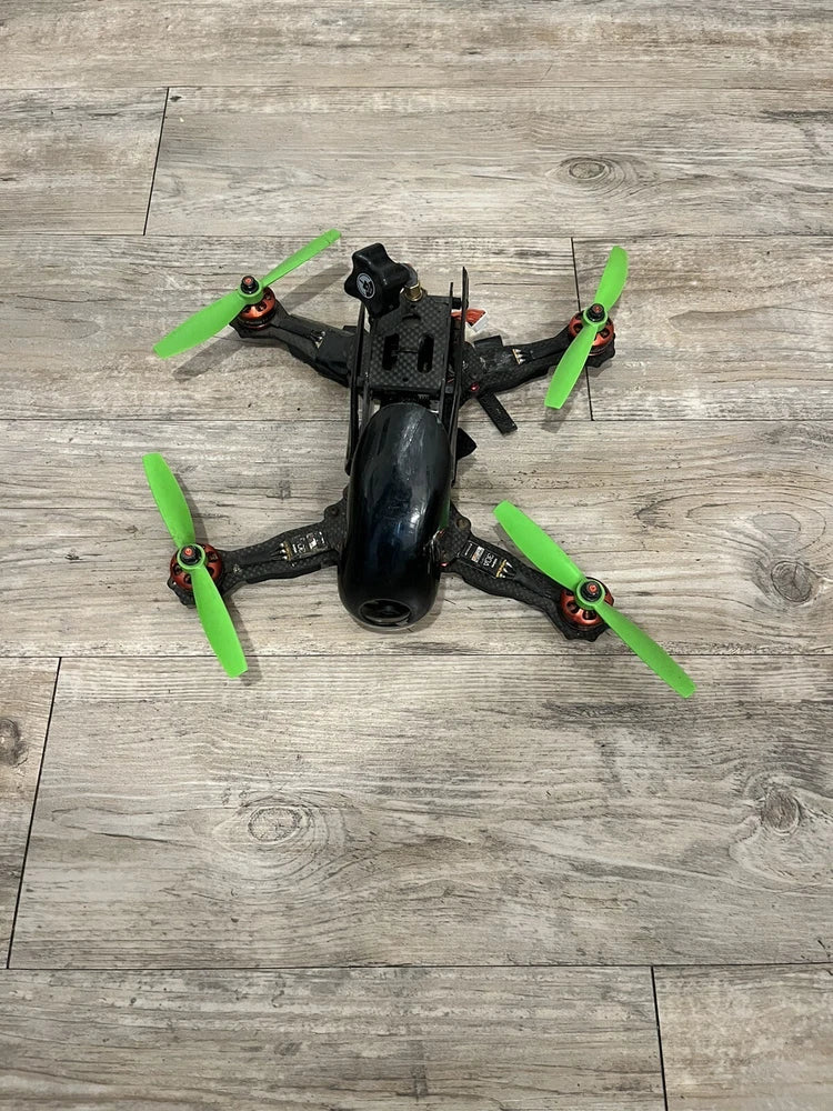 Black racing drone with four green propellers, front view