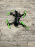 Black racing drone with four green propellers, front view