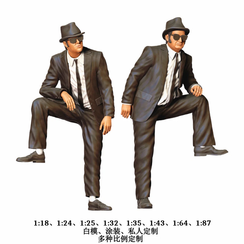 Two black-suit mini male figures with fedora hats and sunglasses, posed seated