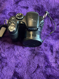 Fujifilm FinePix S1800 digital camera with lens cap and wrist strap, front view