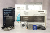 Silver compact digital camera with lens, cables, memory card, and box