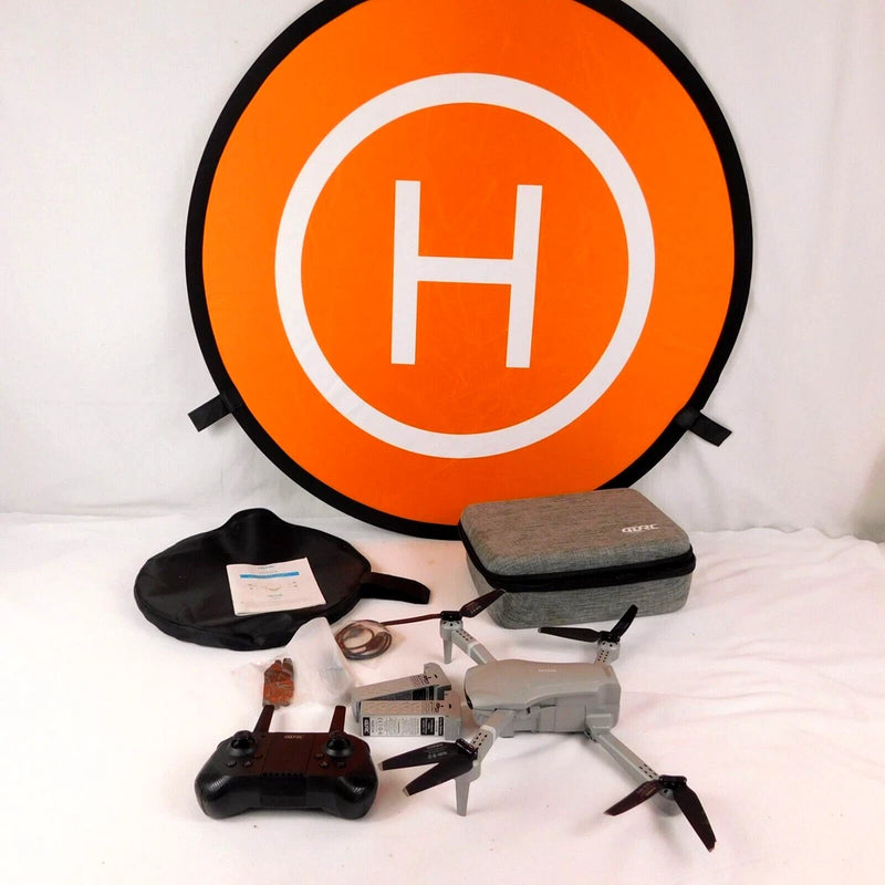 Orange landing target pad with H symbol and gray/black quadcopter drone with accessories