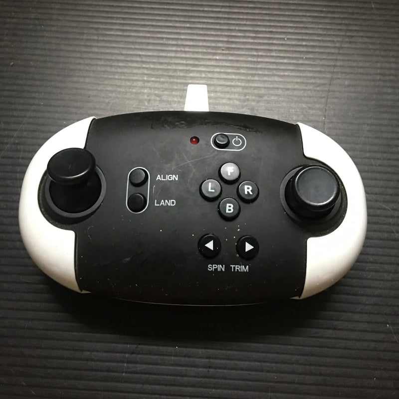 Black drone remote control with two thumbsticks and labeled buttons, power switch