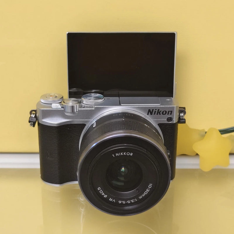 Silver Nikon 1 J5 mirrorless camera with 10-30mm lens, front view