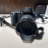 Fujifilm digital SLR camera with attached zoom lens, black body and lens hood strap