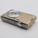 Gold compact digital camera with silver lens ring, front controls and flash