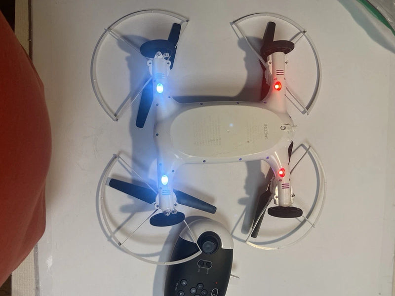 White quadcopter drone with four propellers and blue/red LEDs; handheld controller attached