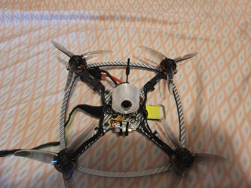 FPV racing drone with open carbon frame, four prop arms, central circular camera.