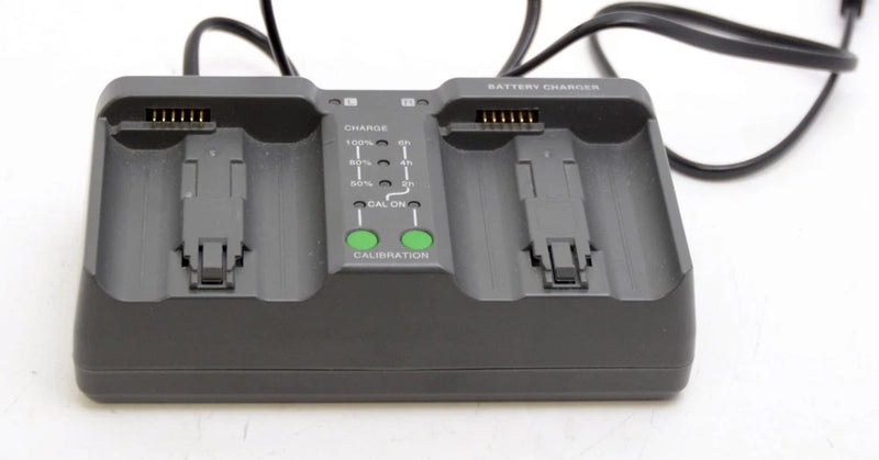 Battery charger base with dual slots and charging contacts, gray plastic.