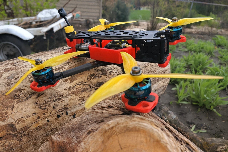 Red and black FPV quadcopter drone with four yellow propellers, on a log outdoors