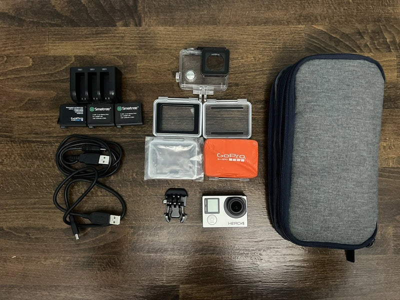 Silver action camera with housing, two mounts, batteries, cables, and grey case