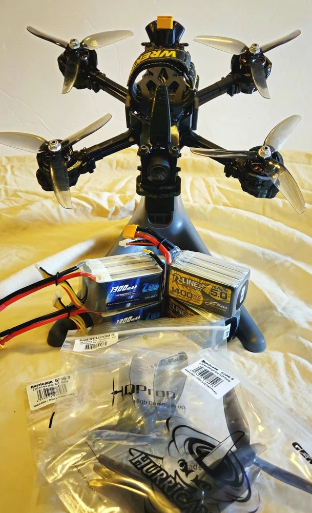 Black quadcopter drone with propellers and accessory batteries in packaging