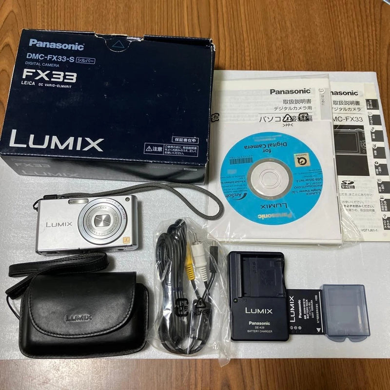 Compact digital camera kit with leather case, lens, battery, cables, and memory card