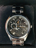 Round analog wrist watch with black face, gold graphics, and silver metal band