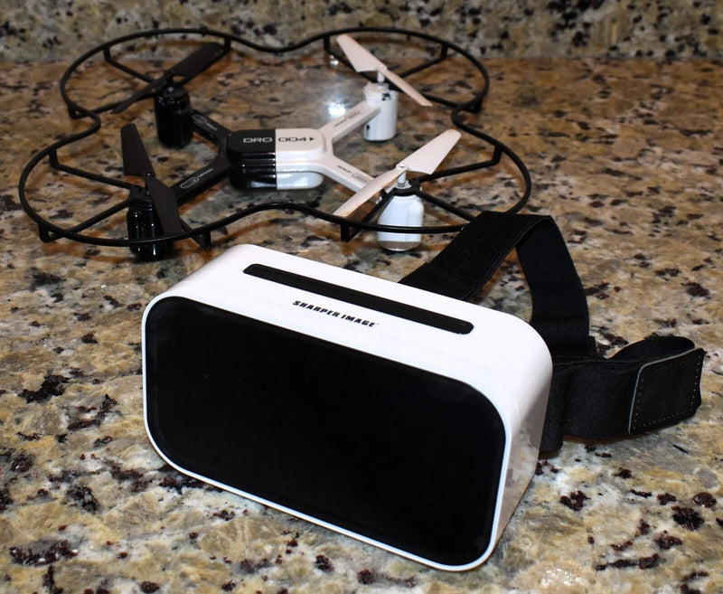 White and black FPV goggles with display window, with small quadcopter nearby