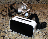 White and black FPV goggles with display window, with small quadcopter nearby