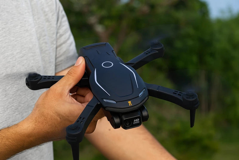 Black quadcopter drone held in hand, with front camera and foldable arms