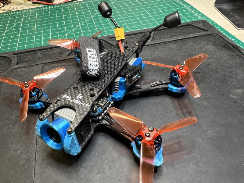 3-inch FPV drone with black carbon frame, orange propellers, and blue motor mounts