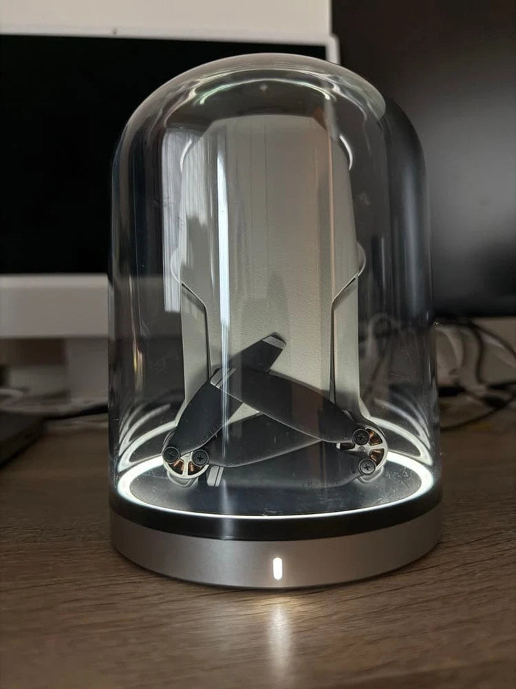 Compact drone under clear protective dome in charging base, front view