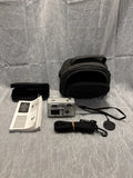 Black digital camera with lens cap, black carrying case, strap, and instruction booklet