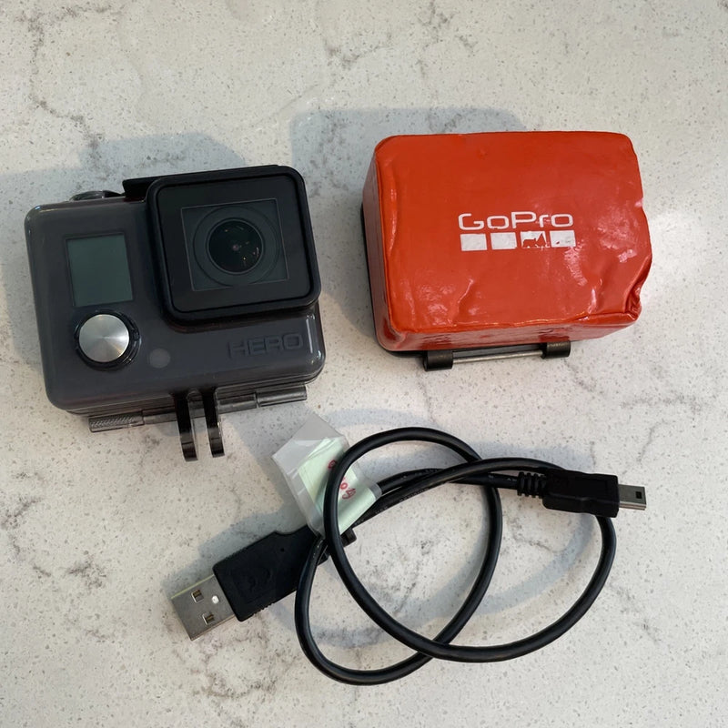 GoPro HERO action camera with gray body, orange case, and USB charging cable