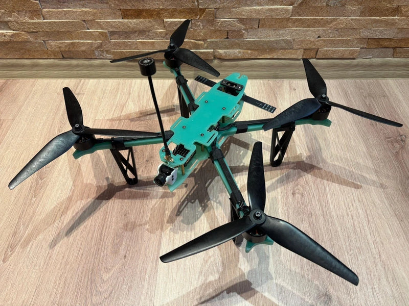 Turquoise FPV drone with five black propellers and central camera mast