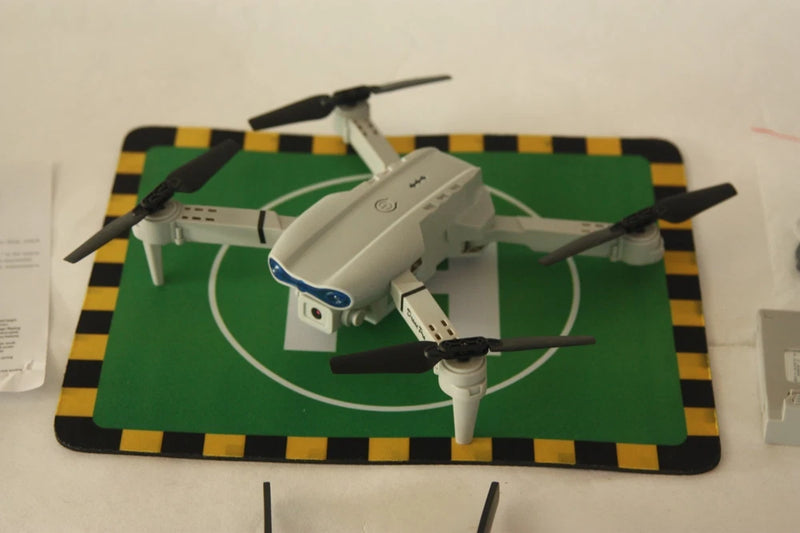 Foldable gray quadcopter drone with 4 rotors, camera body, arms folded.