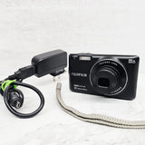 Black Fujifilm FinePix compact digital camera with lens, flash, and power adapter
